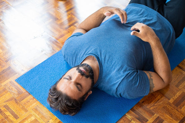 Man lying on a yoga mat with a hand on his chest doing breathwork