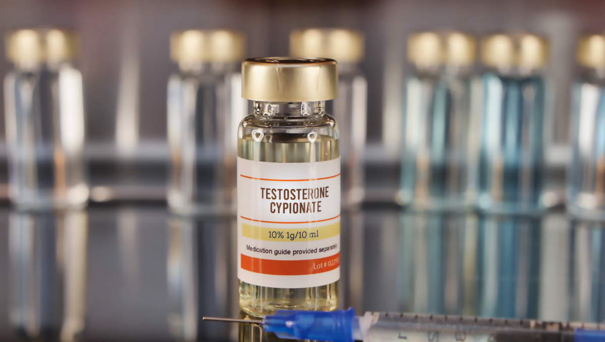 Vial of testosterone cypionate with syringes in the background